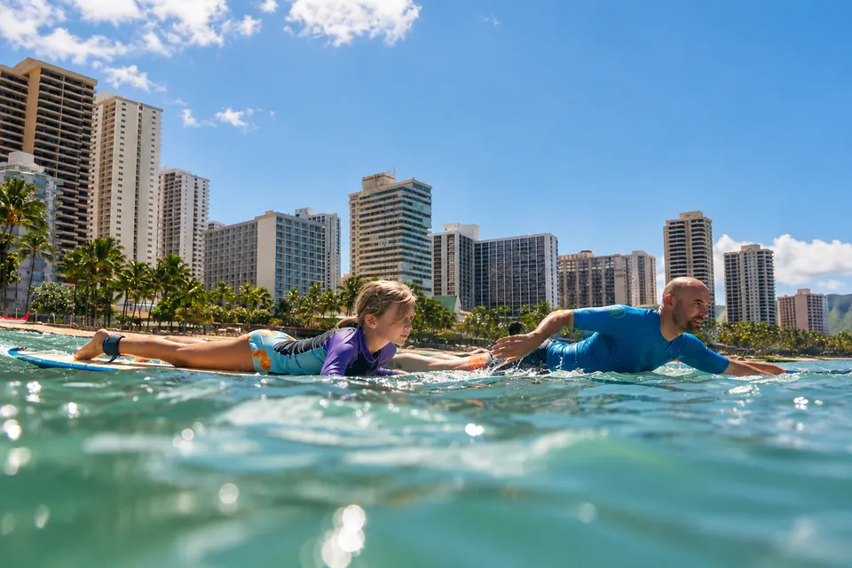 A surf instructor and a young student paddling out together off Waikīkī